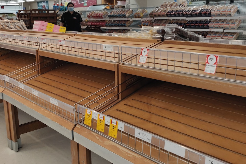 An empty shelf with breadrolls in the neighbouring shelves. 