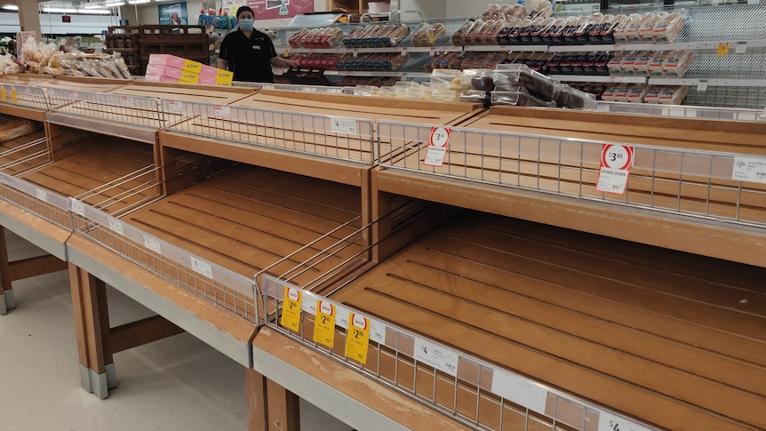 An empty shelf with breadrolls in the neighbouring shelves. 