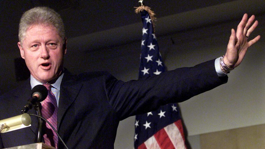 Bill Clinton speaks in front of a US flag.