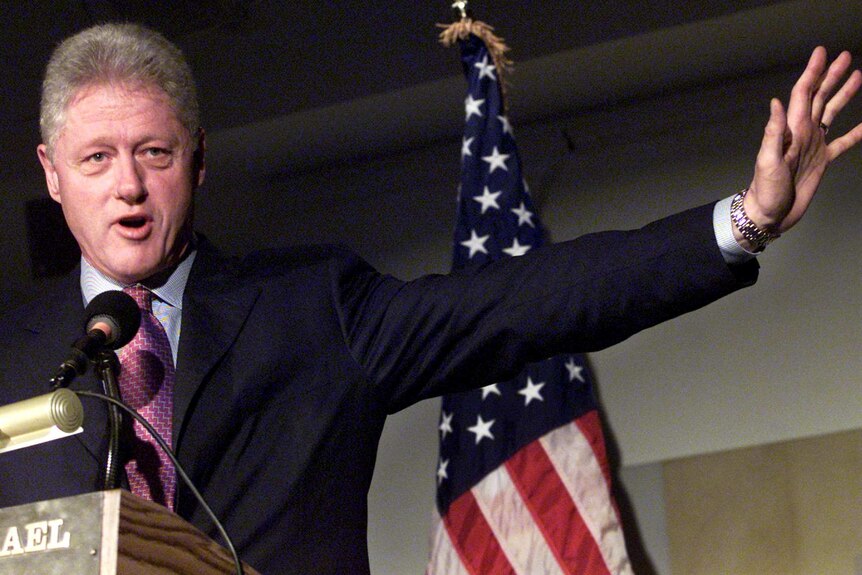 Bill Clinton speaks in front of a US flag.