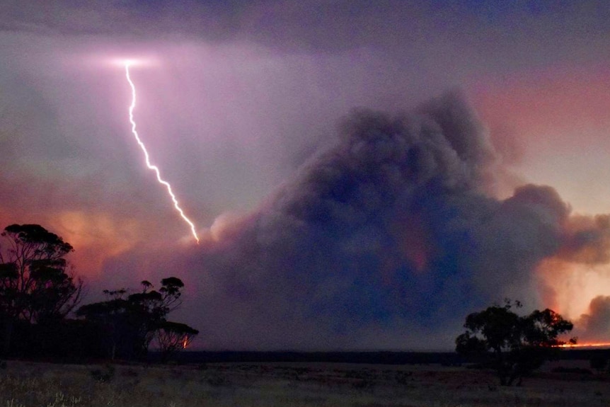 An lightning bolt strikes a cloud of smoke from a fire burning on a wheat field at low light.