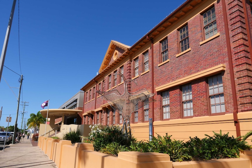 an old brick building on a sunny day with a bird statue out the front and a Queensland flag flying