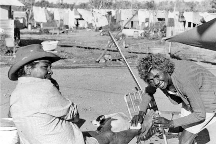 A young woman tends to a wound on a man's leg. She is smiling to the camera.