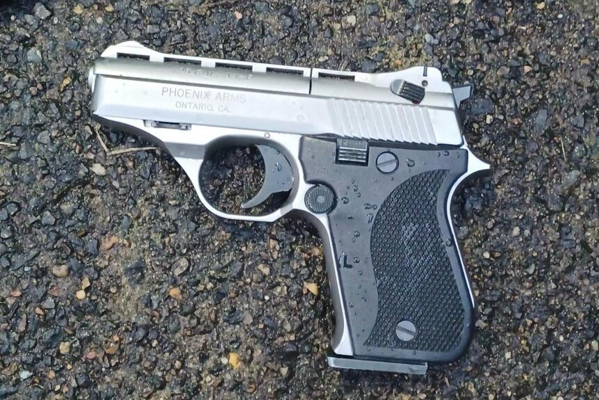 A silver and black gun lying on a gravel driveway