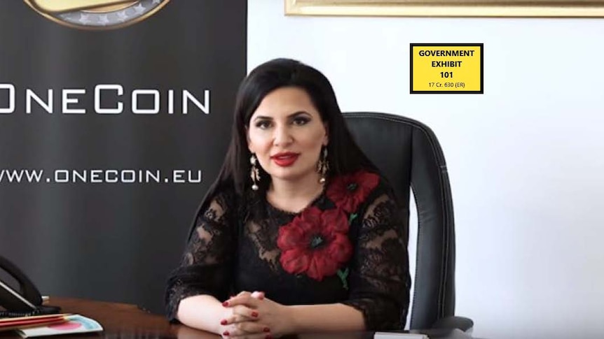 A woman sitting in front of a sign which says OneCoin. 