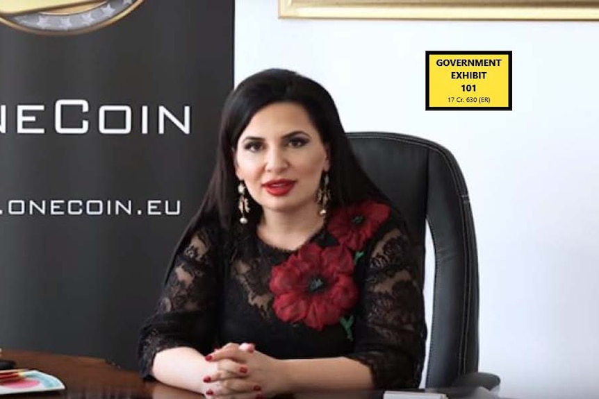 A woman sitting in front of a sign which says OneCoin. 