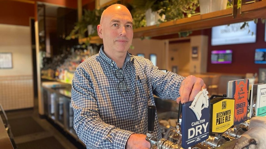 bald man in blue check shirt pouring a beer from the tap