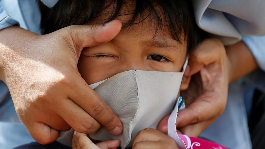 An Indonesian child has a protective face mask adjusted.