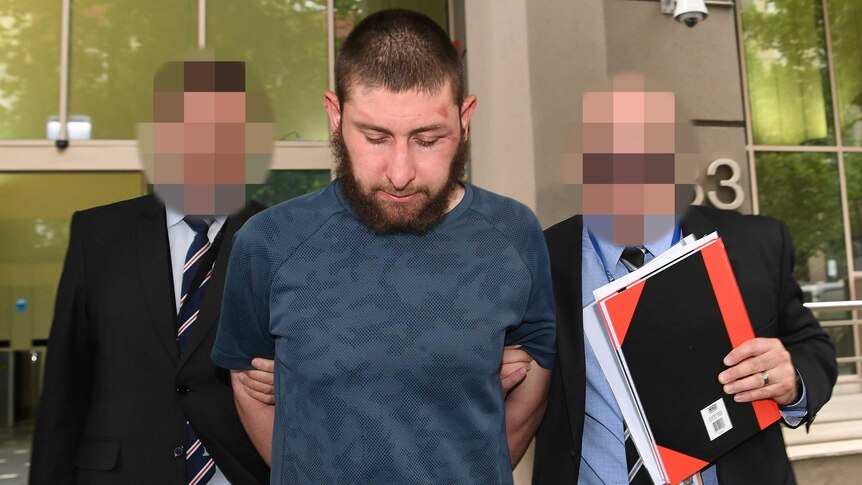 A front on shot of the bearded suspect flanked by two AFP officers, whose faces are pixelated.