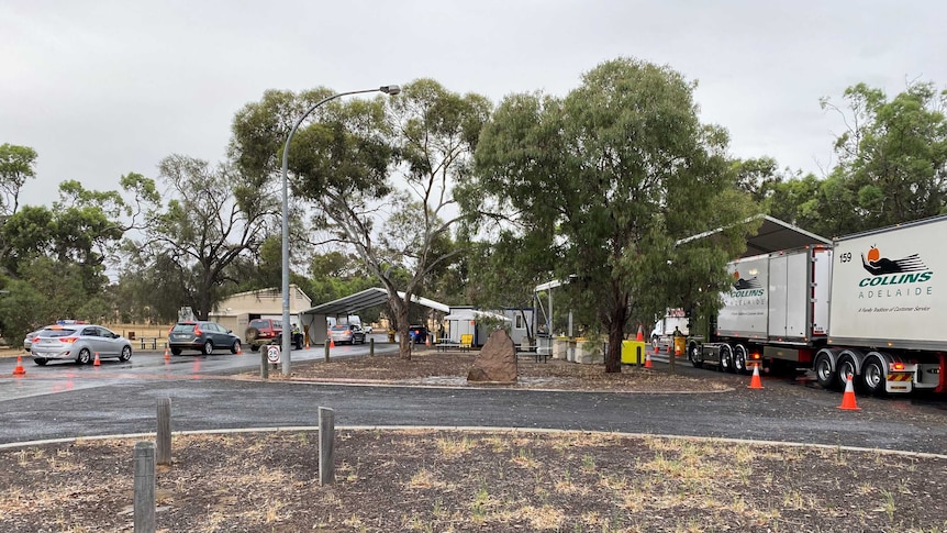 cars and trucks line up on a country road, queuing for the checkpoint shed