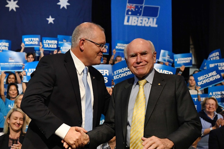 A balding middle-aged man in a suit shakes the hand of an older, shorter man at a political rally.