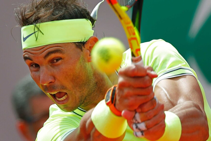 Rafa Nadal opens his mouth and uses both hands to hit the ball wearing a yellow top