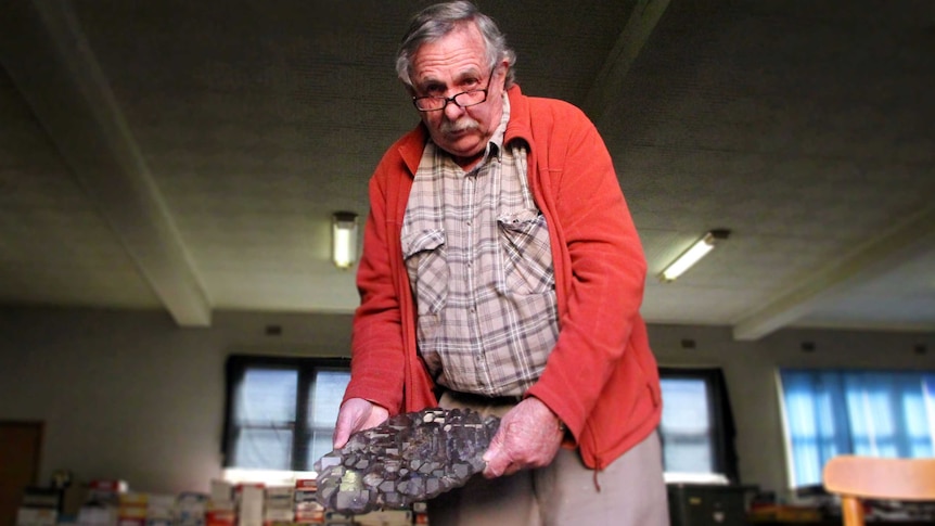 A man holds a mineral specimen, transparent, shiny prisms smoky lavender in colour.
