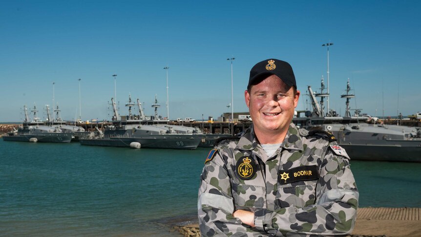 Navvy leading seaman standing in front of Darwin Waterfront with navvy vessels in background.