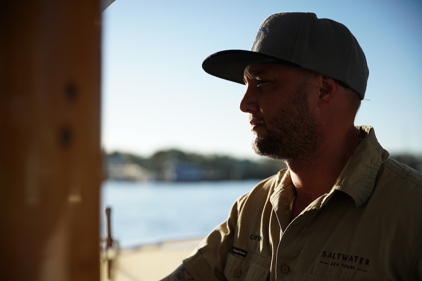 A close-up shot of a man, wearing a baseball cap and khaki shirt.