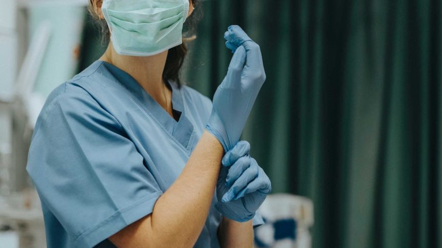 A masked nurse adjusts their blue plastic glove in an operation room