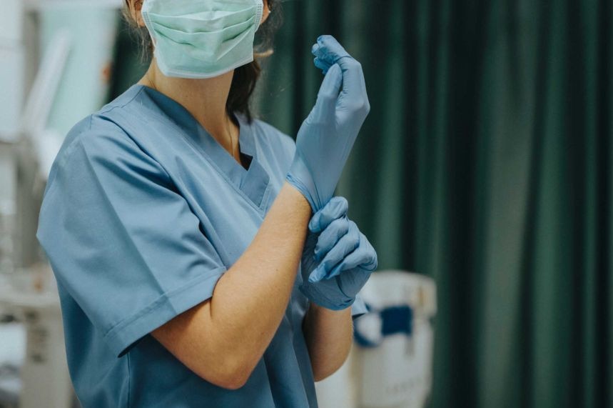 A masked nurse adjusts her blue plastic glove in a surgery theatre.
