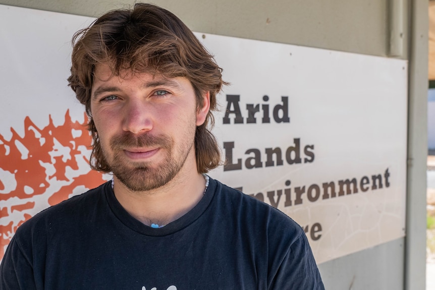 chest high photo of man with beard in frobt of arid lands management   sign