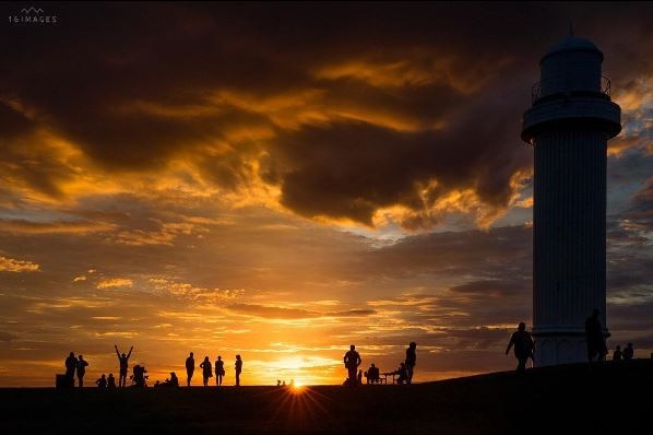Sunrise at Wollongong's Flagstaff Hill with lighthouse and people in silhouette.