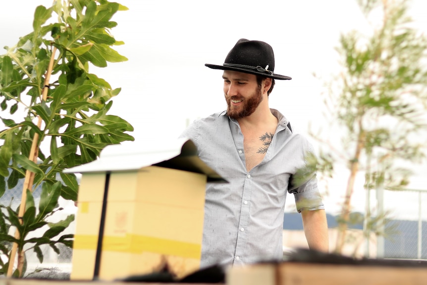 Conor wears a wide brimmed hat and grey button-up shirt while watering plants.