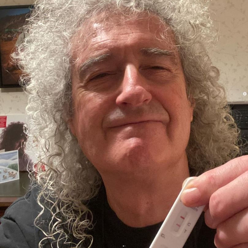 Brian May holds up a rapid antigen test in a selfie.