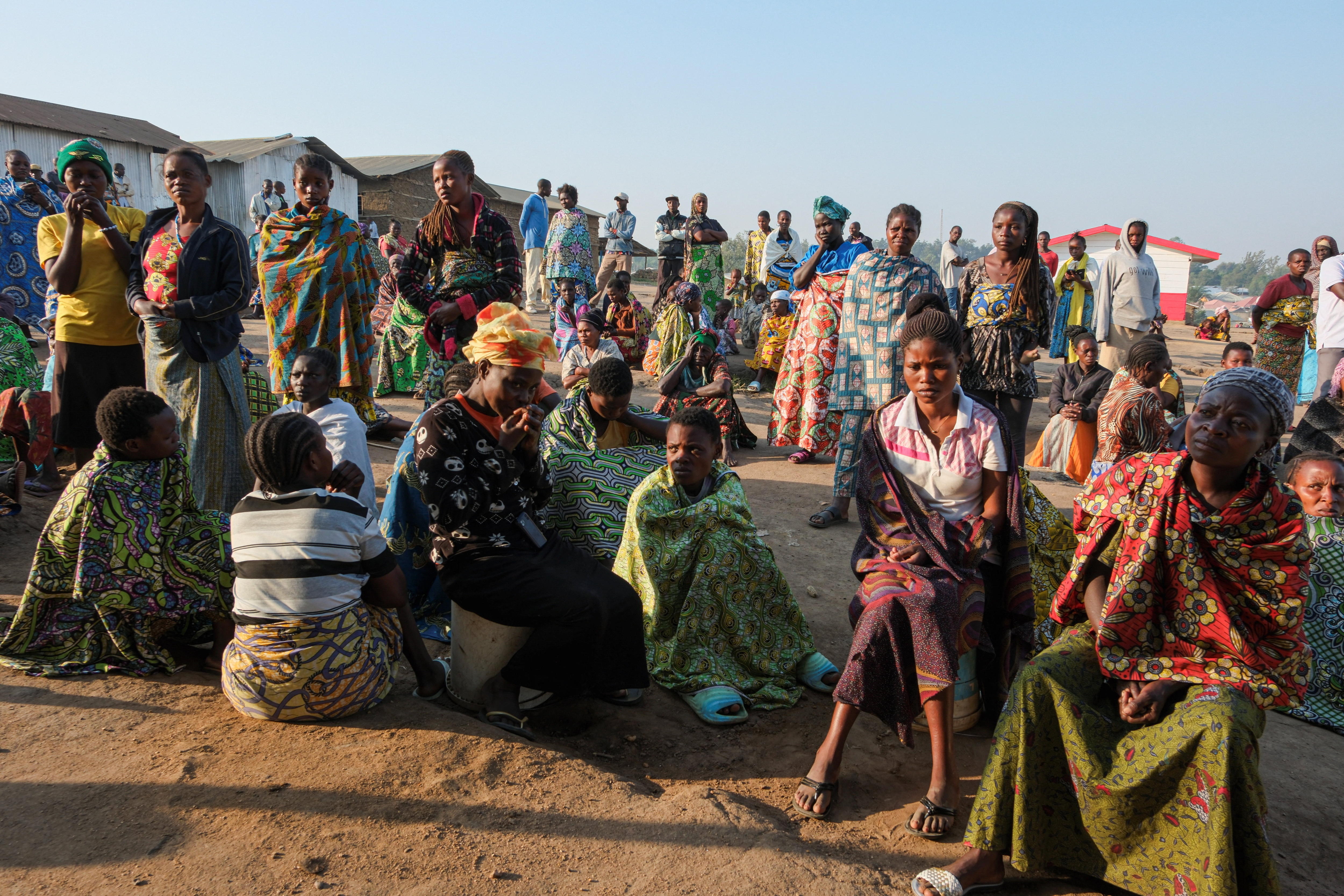 A large group of Congolese people, mostly women in bright clothing, gather in a refugee camp.