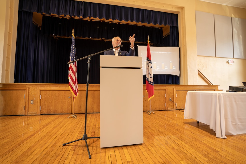 A man in a suit at a lectern points his finger 