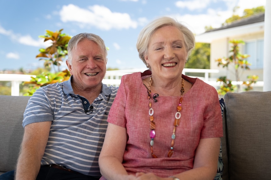 A man and a woman sit on a couch outdoor.