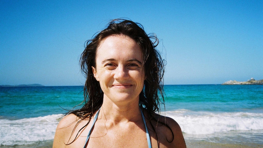 A woman smiles in front of waves at a beach.