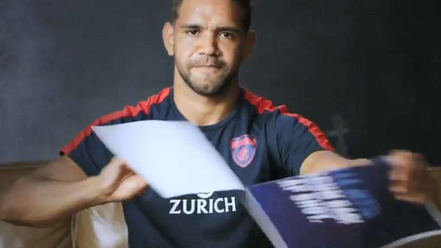 Melbourne football player Neville Jetta tears a sign showing an abusive tweet about him.