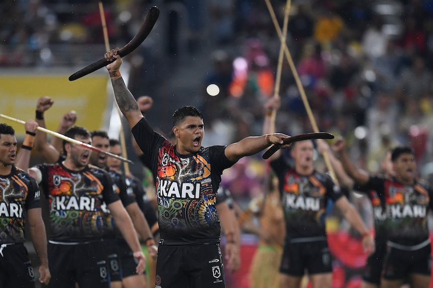 An Aboriginal rugby league player holds up two boomerangs during a pre-match war cry performance