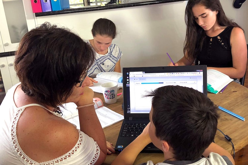 Mother Michelle House looks at her three children sitting at table and studying during home schooling session.