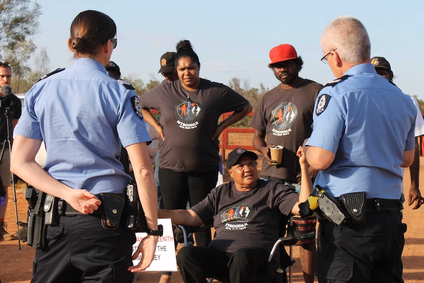 Image of police officers speaking to protesters on the road to an isolated cattle station.