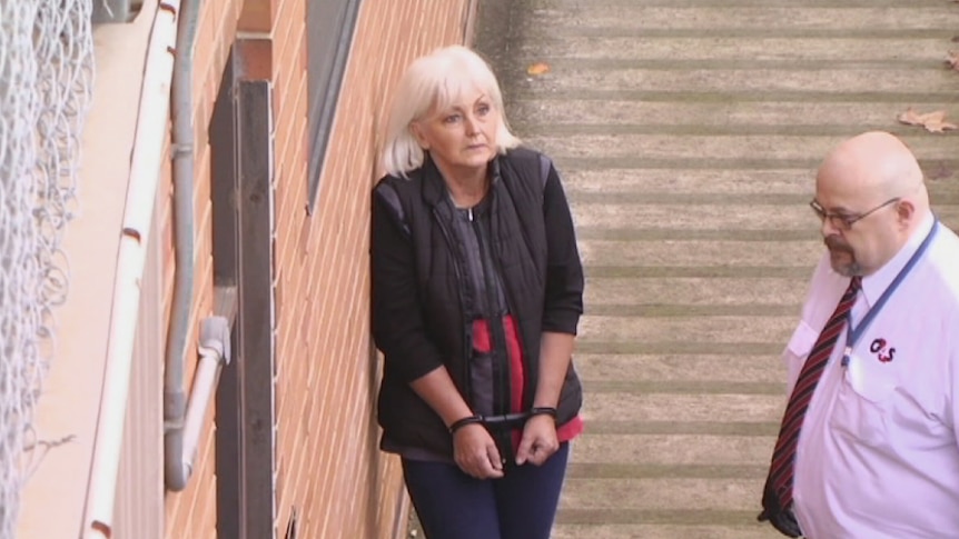 Accused woman in handcuffs at court, with a court officer nearby.