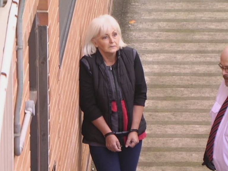 Accused woman in handcuffs at court, with a court officer nearby.