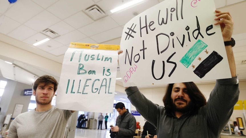 Protesters hold signs saying "he will not divide us" in response to Trump immigration ban