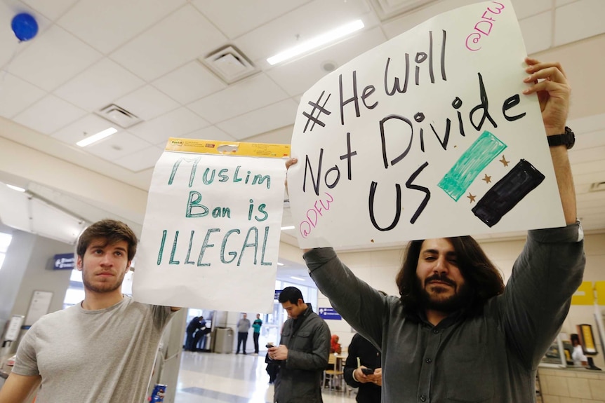 Protesters hold signs saying "he will not divide us" in response to Trump immigration ban