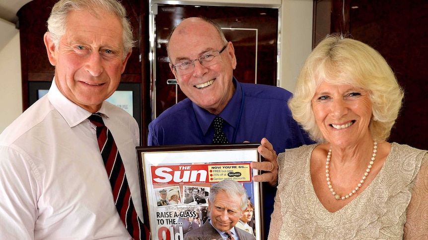 Arthur Edwards, standing between Prince Charles and Camilla, holds a framed front page of the Sun newspaper.