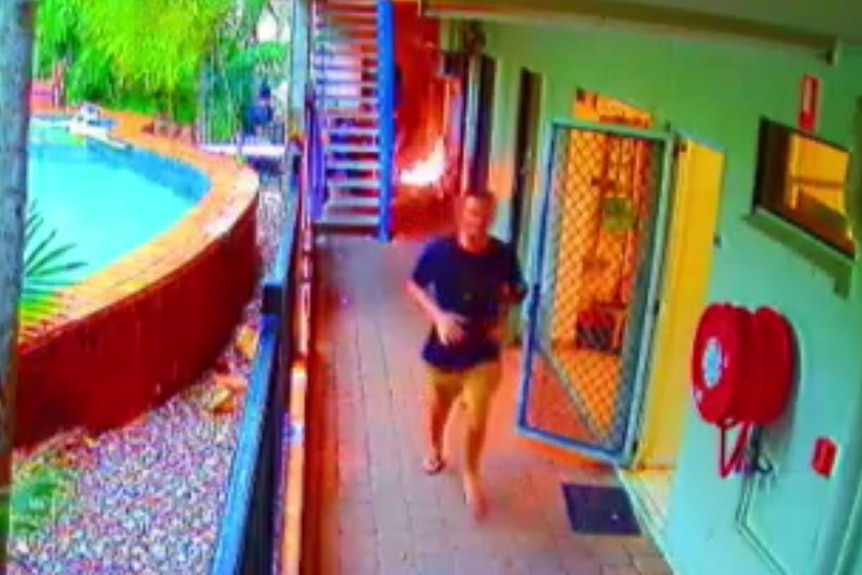 A CCTV still showing a man running along a path at a hostel, away from a fire behind him.