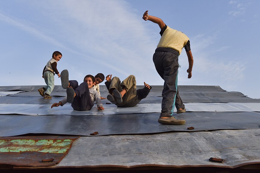 Children slide down a roof covered in sheets of metal.