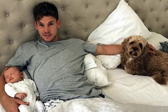 Jack Redden in bed with his baby in one arm and the other on the family dog.