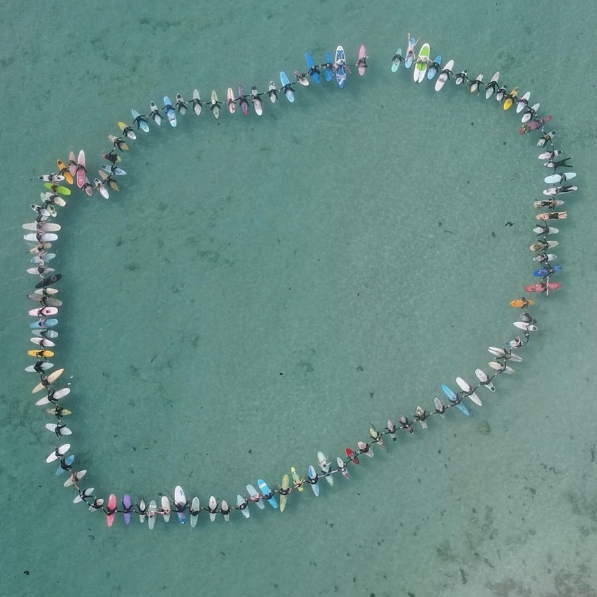 Aerial photo of surfers on boards in circle joining hands  