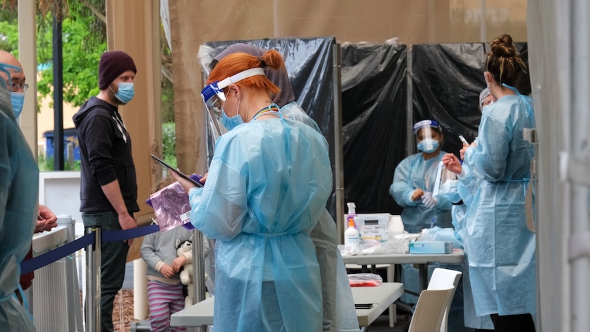 Five health workers in full PPE masks and gowns at a COVID testing centre.