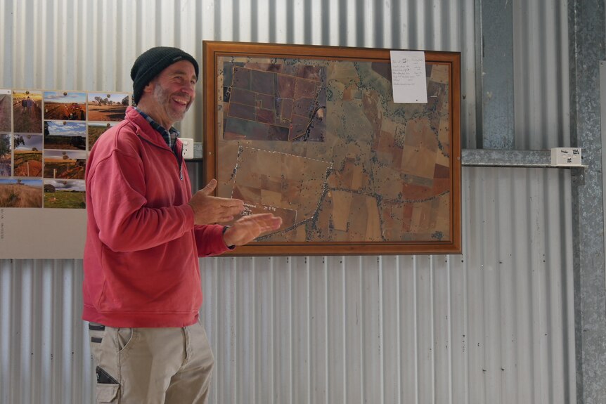 A man in a red shirt standing in front of a map of his farm 
