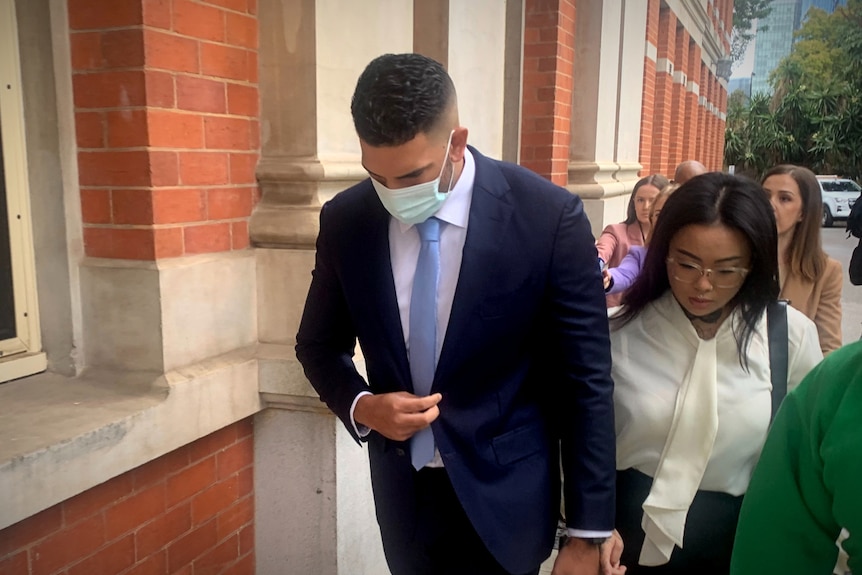 A man dressed in a blue suit, white shirt, tie and face mask walks outside the Supreme Court in Perth, with a woman on his left.