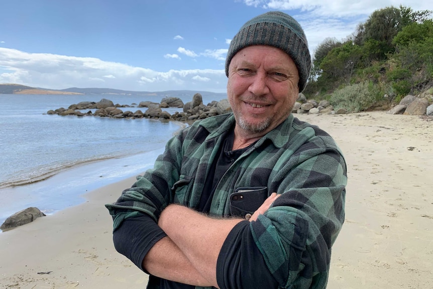 A man crosses his arms and smiles at the beach