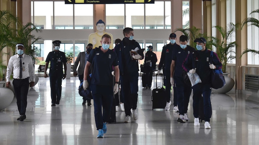 A group of cricket teammates wearing masks and gloves walk through an international airport.