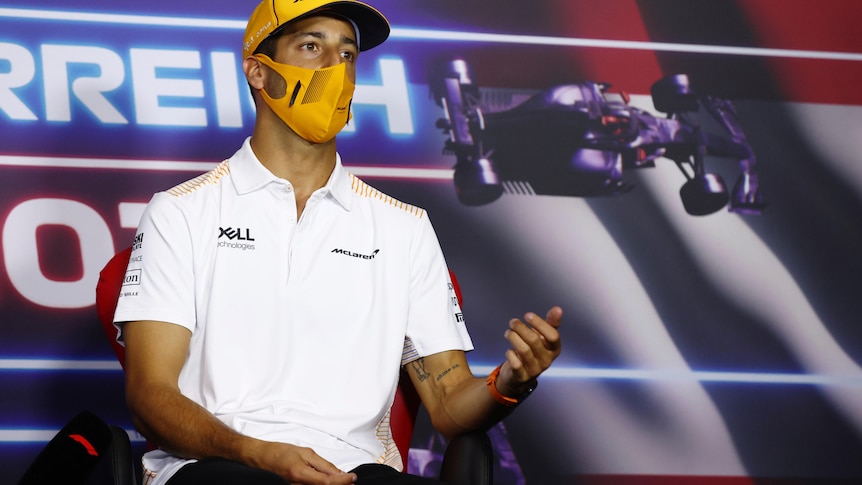 A mask-wearing Daniel Ricciardo gestures with his hand as he makes a point at an F1 press conference.