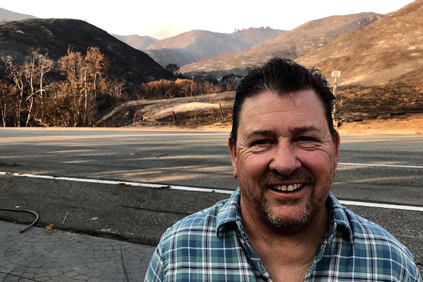 A man stands next to a road with charred landscape behind him