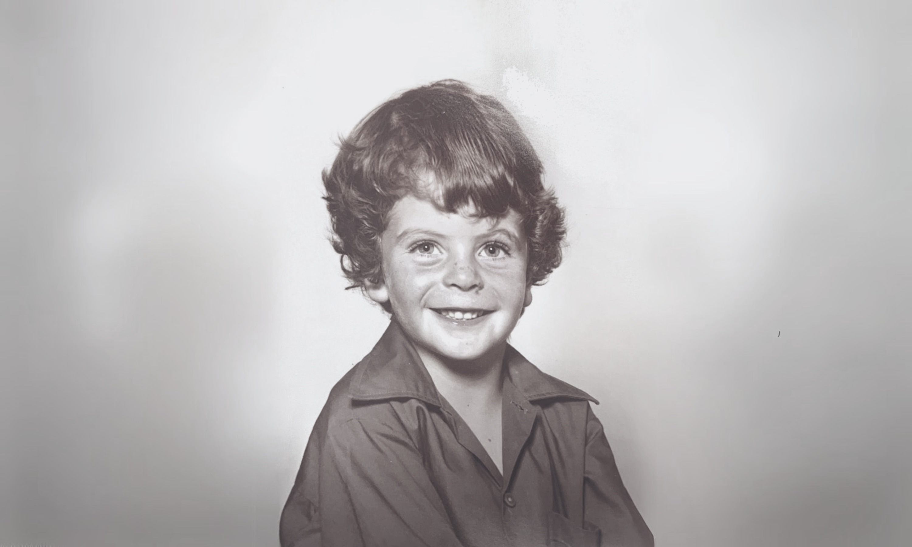 Sepia-coloured school photo of smiling four year old boy in a school uniform